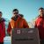 Models showcasing premium Canadian winter jackets in a snowy landscape with a parcel displaying a ShipByMail.com label, symbolizing shipping from Canada to USA.